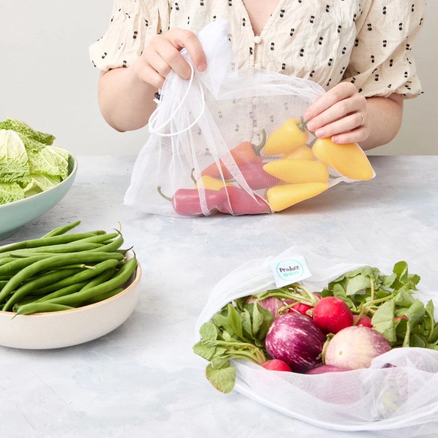 Person holding a reusable mesh produce bag filled with mini-capsicums on a table