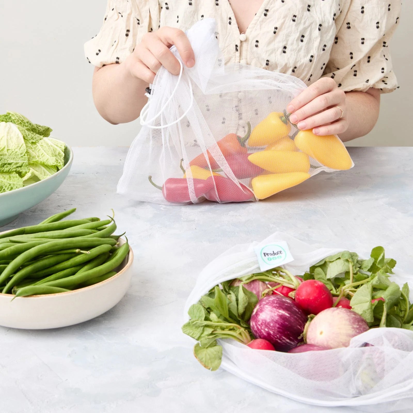 Person holding a reusable mesh produce bag filled with mini-capsicums on a table