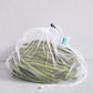 White drawstring mesh reusable produce bag filled with green beans on a light grey background