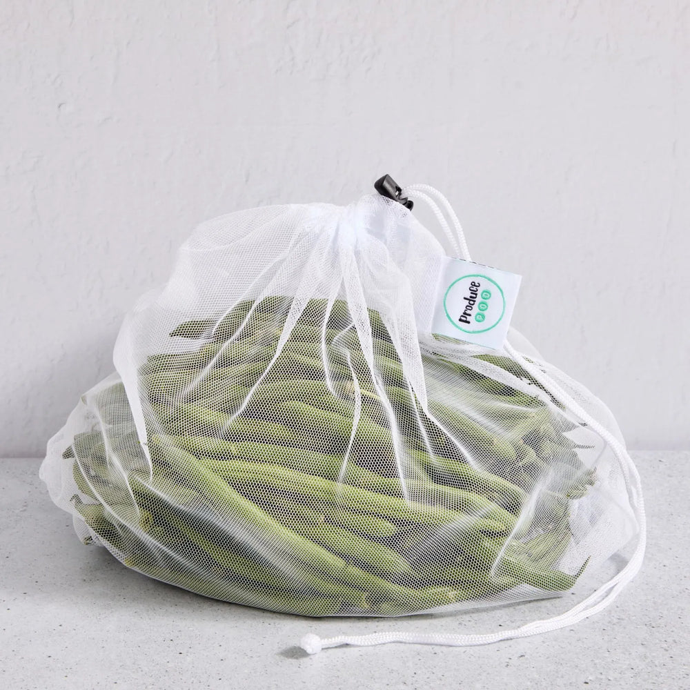 White drawstring mesh reusable produce bag filled with green beans on a light grey background